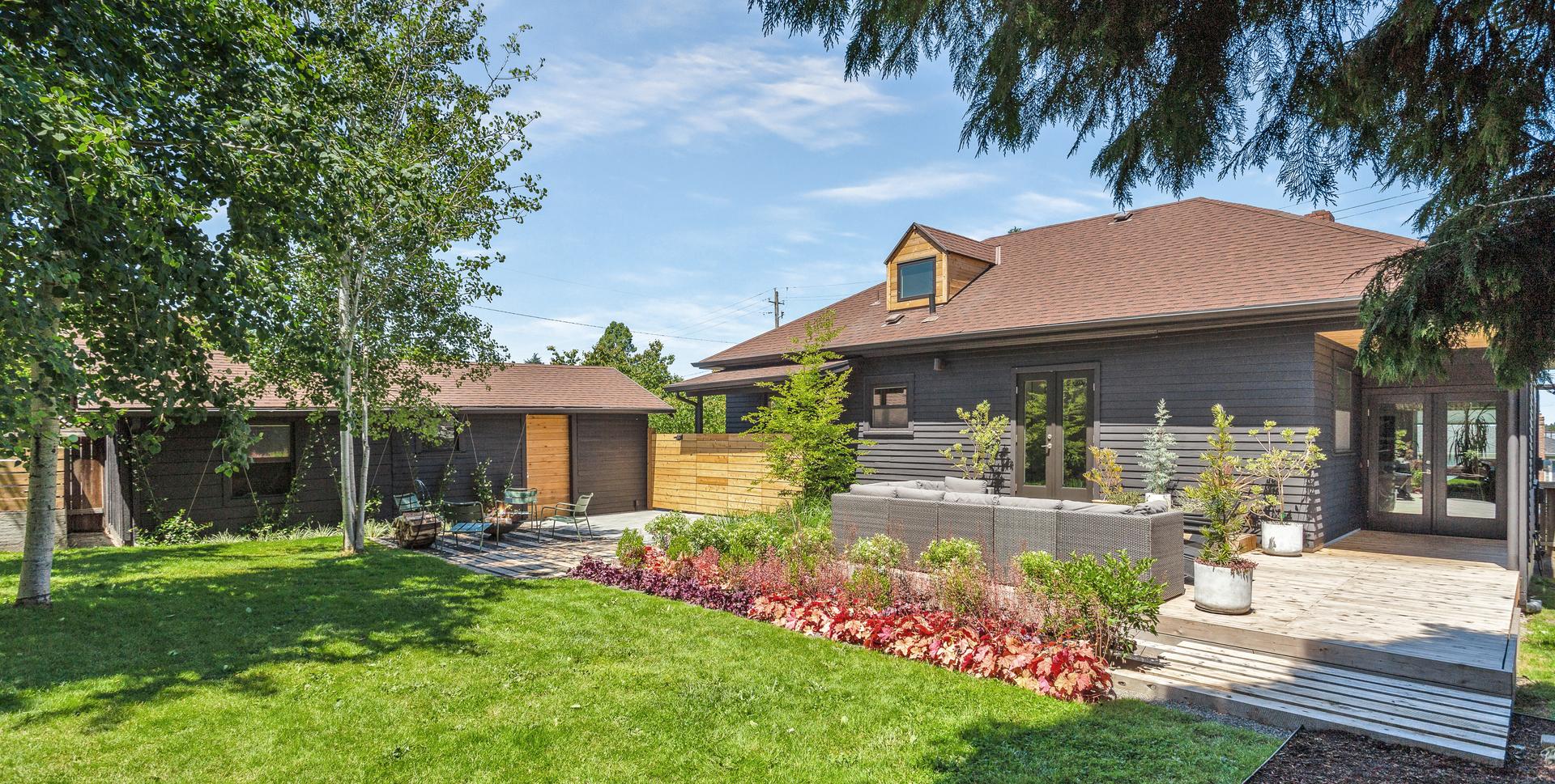View of the back of the house with deck, patio, trees, and plantings at a private residence in Portland.