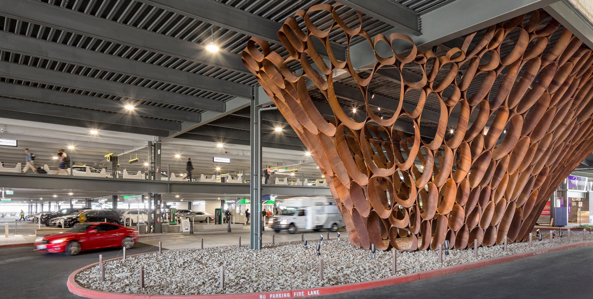 Sculptural wood installation shaped like a tree trunk under the PACR structure near the arrivals area.
