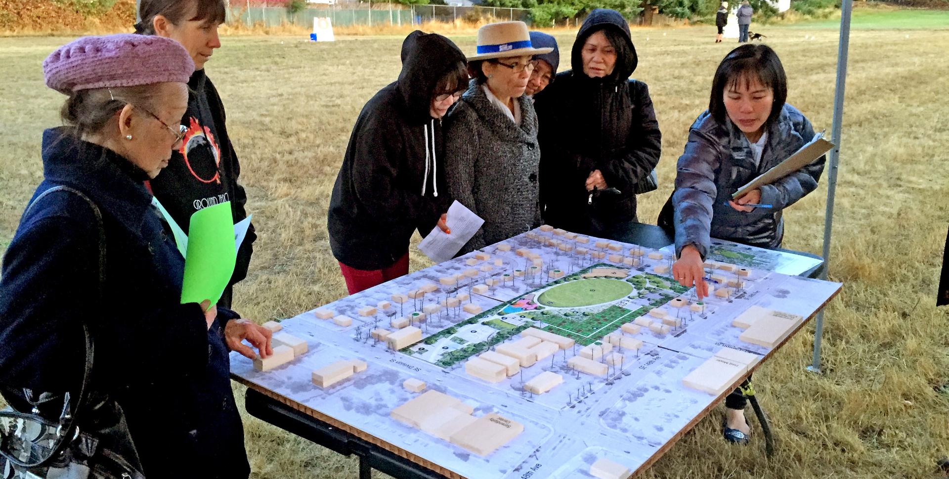 Community members gathered around a site model at an outdoor planning event.