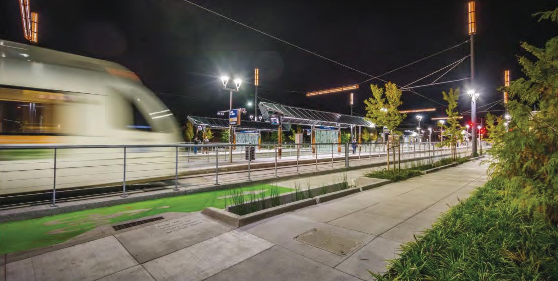 MAX Orange Line train passing a station at night with illuminated landscaping.