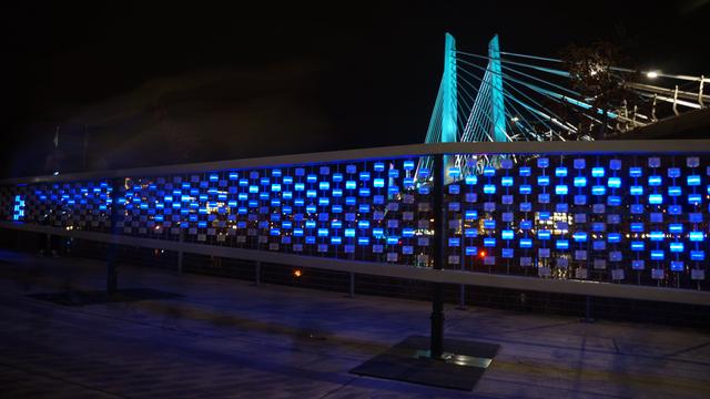 Interactive light installation with glowing blue skateboard wheels along the Portland waterfront at night.