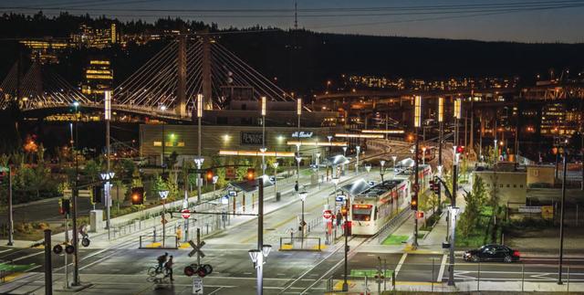 Night view of the MAX Orange Line light rail at Tilikum Crossing with the bridge and city lights in the background.